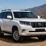 SUV blanc garé sur une piste au-dessus de la côte atlantique, montagnes arides en arrière-plan